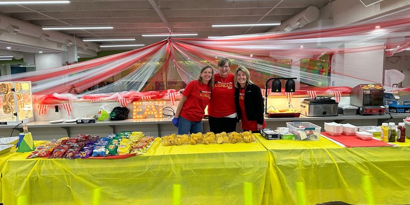 After Prom carnival decorations are a table with food, 3 volunteers standing behind table