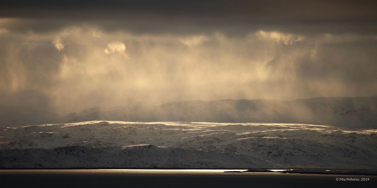snow dusting distant mountains, sun shining through clouds on a slate grey sea. Frobisher bay, Baffi