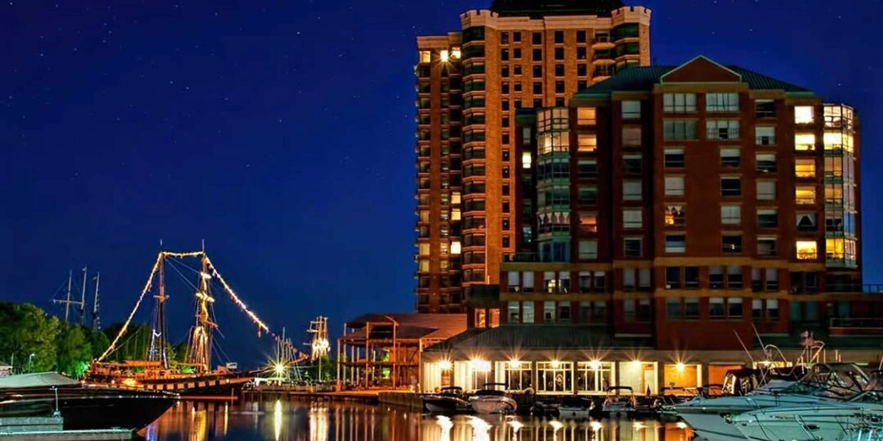Night view of a marina with illuminated boats and buildings reflecting on the water.