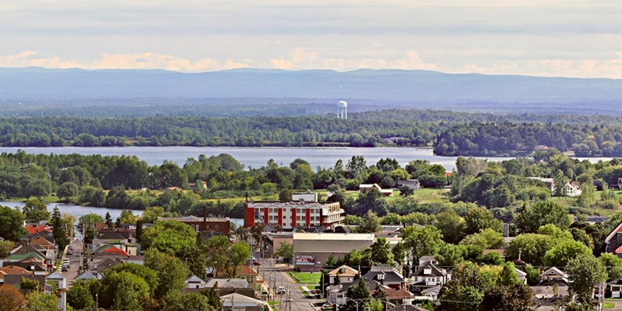 A panoramic view of a small town with a river and distant mountains.