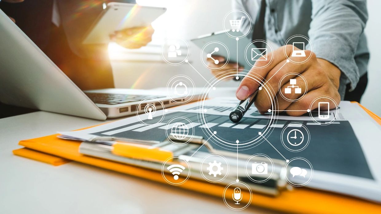 Person analyzing data on paper with digital icons overlay and devices nearby.