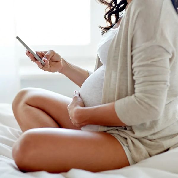 pregnant woman sitting on bed with her cellphone