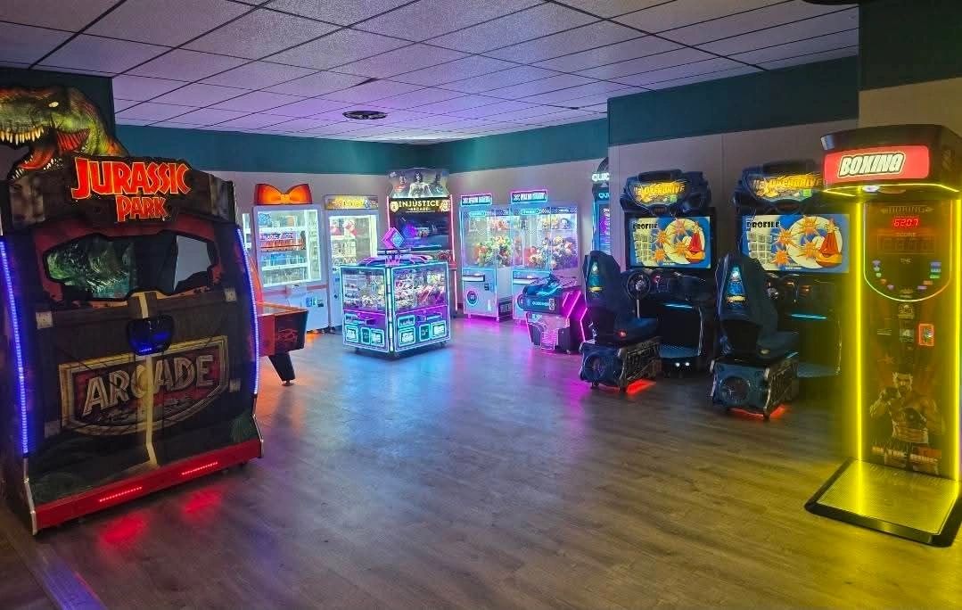 A colorful arcade room with various game machines including Jurassic Park and boxing.