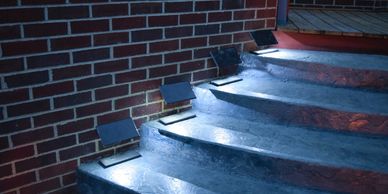 A night photo of four Step Edge Lanterns located on a patio stairway.