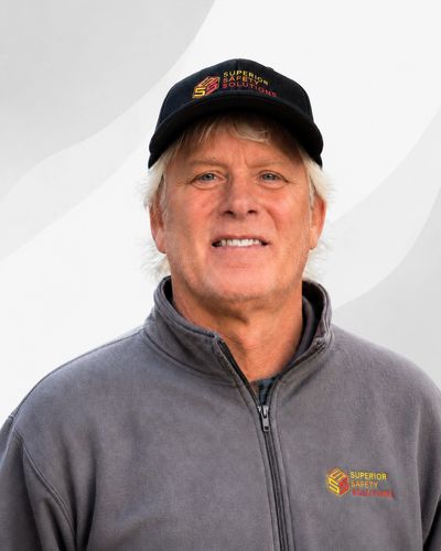 Man in a gray jacket and black cap with company logos.