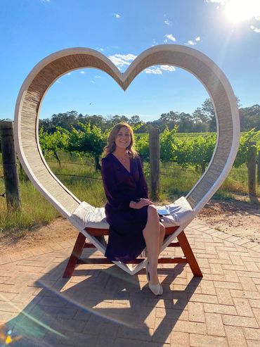 Woman sitting on a heart-shaped chair outdoors on a sunny day.