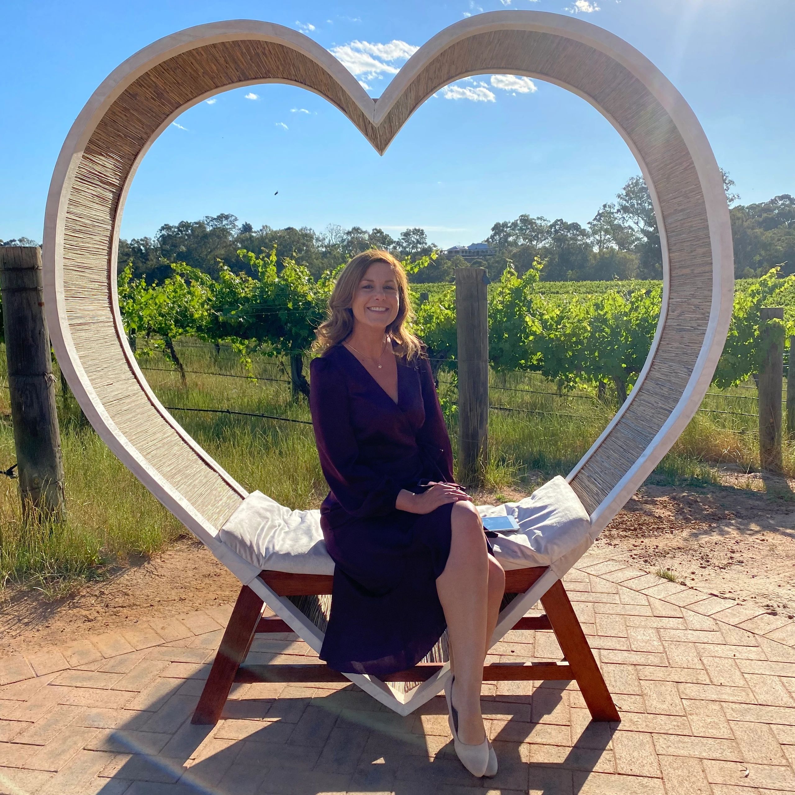 Woman sitting on a heart-shaped swing on a sunny day.