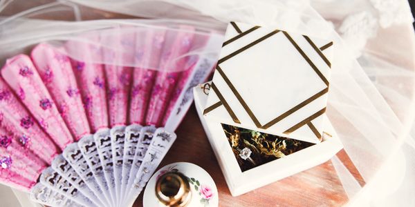 Decorative pink fan and elegant jewelry box with ring inside on a soft fabric.