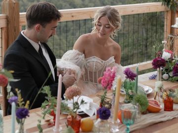 A couple dressed elegantly, sharing a moment at a beautifully decorated outdoor table.