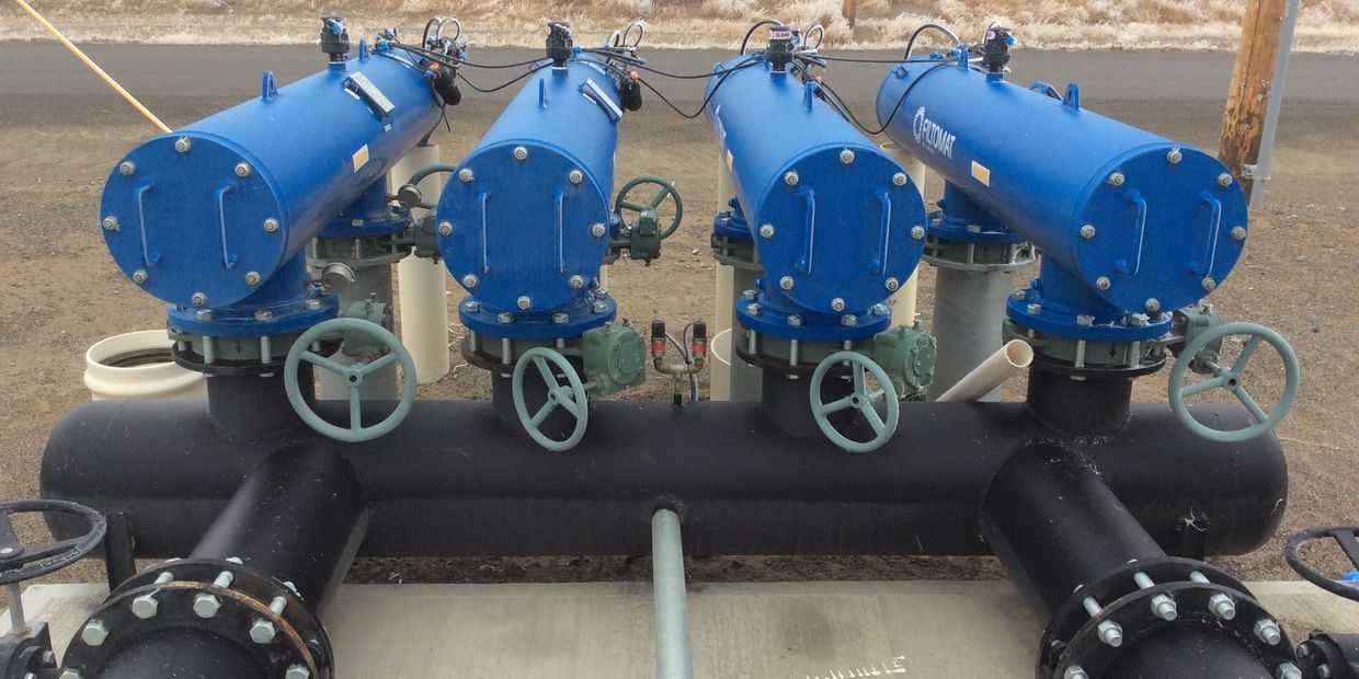 Four blue industrial filters with handwheel valves on a black pipe manifold.