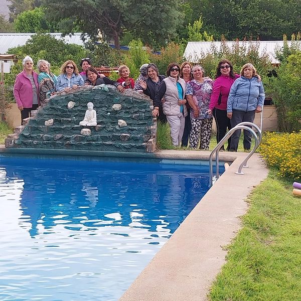 An outdoor photo featuring a group of twelve smiling older women posing behind a rock formation