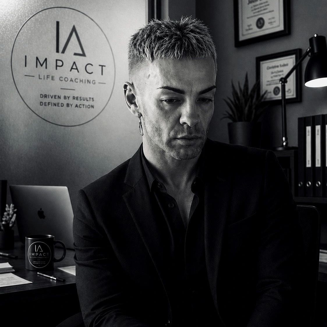 A man in a suit sits thoughtfully in a coaching office with Impact Life Coaching branding.