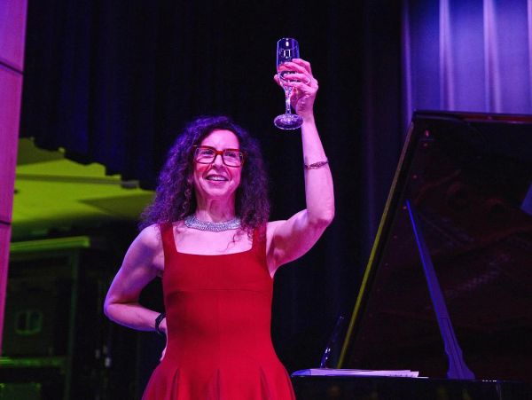 Woman in red dress raising a glass on stage.