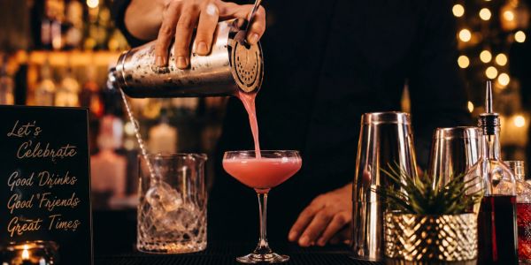 Bartender sirviendo un cóctel rosado en un bar.