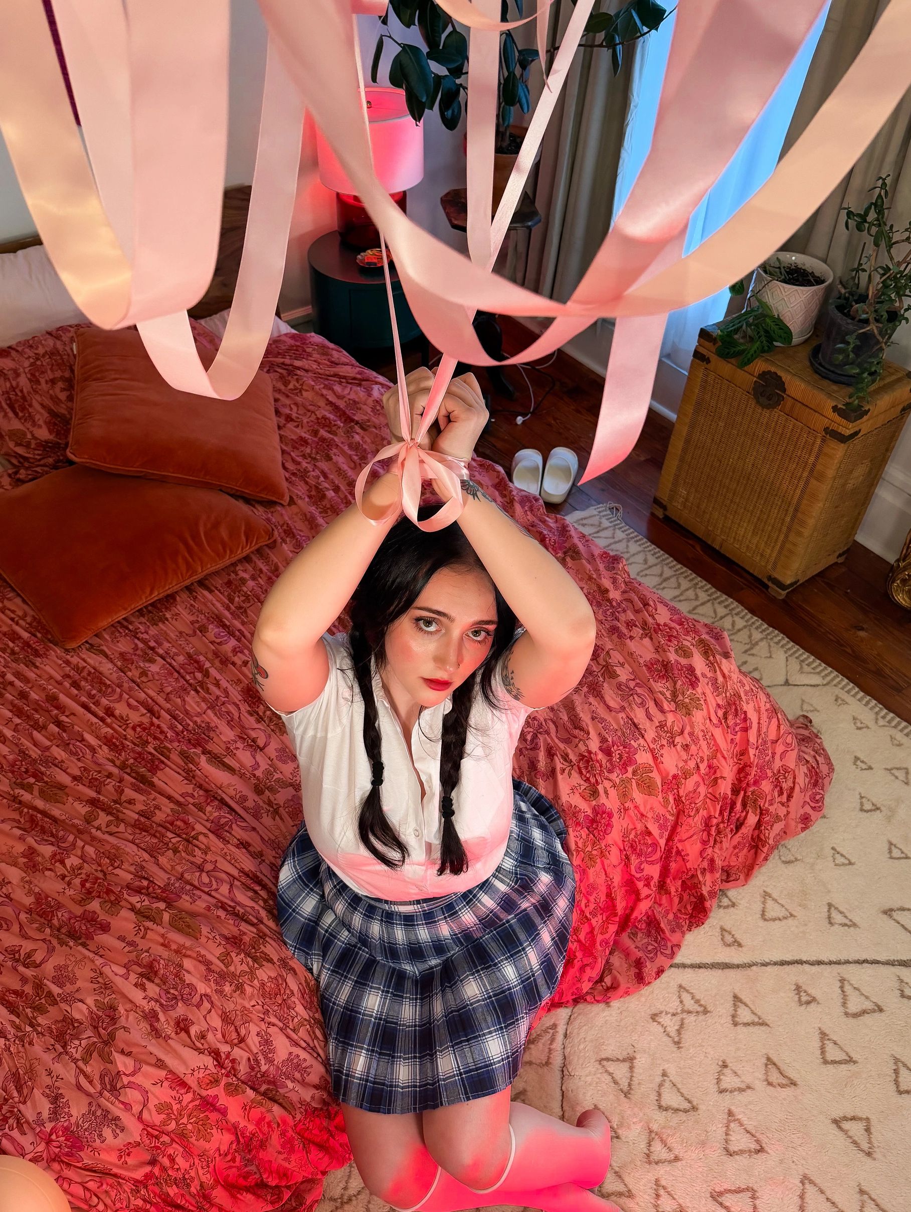 Woman tied to ribbons above bed, looking up.