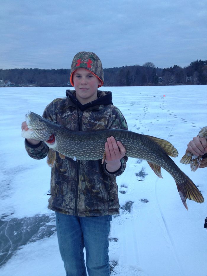 Boy holding a large fish on a snowy frozen lake.