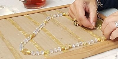 Hands stringing a necklace with yellow and clear beads.