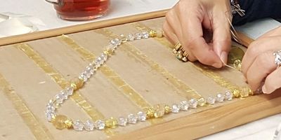 Hands stringing a necklace with yellow and clear beads.