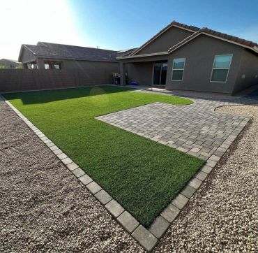 Modern backyard with artificial grass and stone patio under clear blue sky.