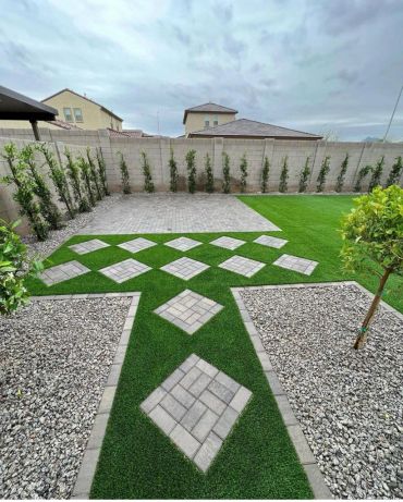 Modern backyard with geometric stone and grass design, surrounded by small trees and stone beds.