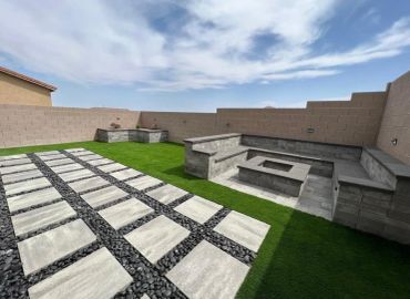 Modern backyard with stone seating and fire pit under blue sky.