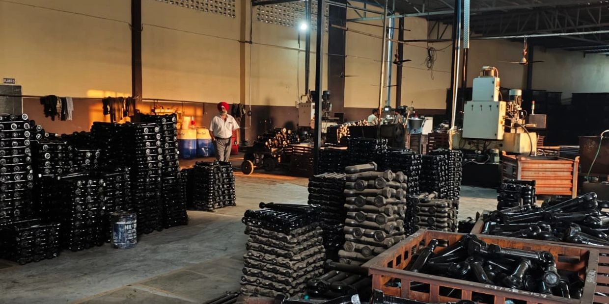 Factory interior with stacks of tines, forged hooks, springs parts and workers in the background.