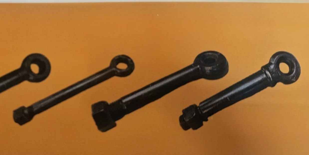 Four black eye bolts with nuts on an orange surface.
