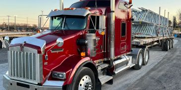 Camion rouge avec remorque transportant des structures métalliques.