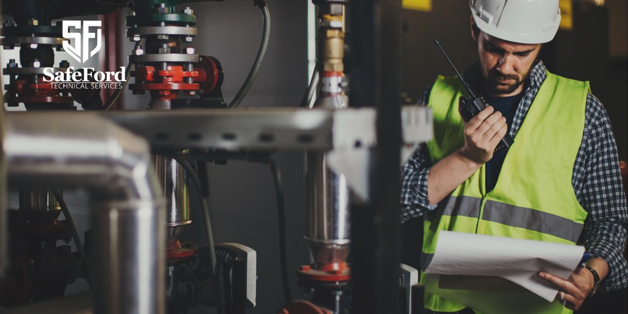 Engineer in safety vest and helmet inspecting pipes and holding a walkie-talkie.