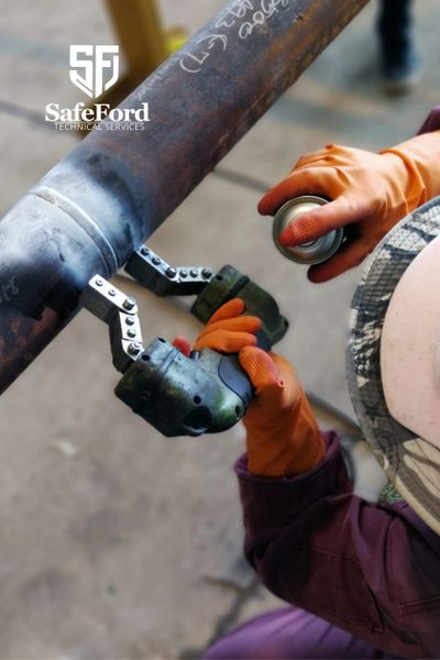 Technician inspecting pipe weld with protective gloves and spray can.