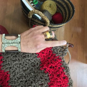 A person sitting crocheting a scarf with a basket of yarn on the floor. 