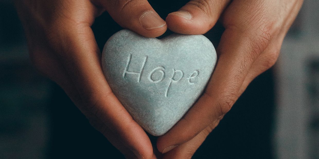 Hands holding heart-shaped stone inscribed with the word hope