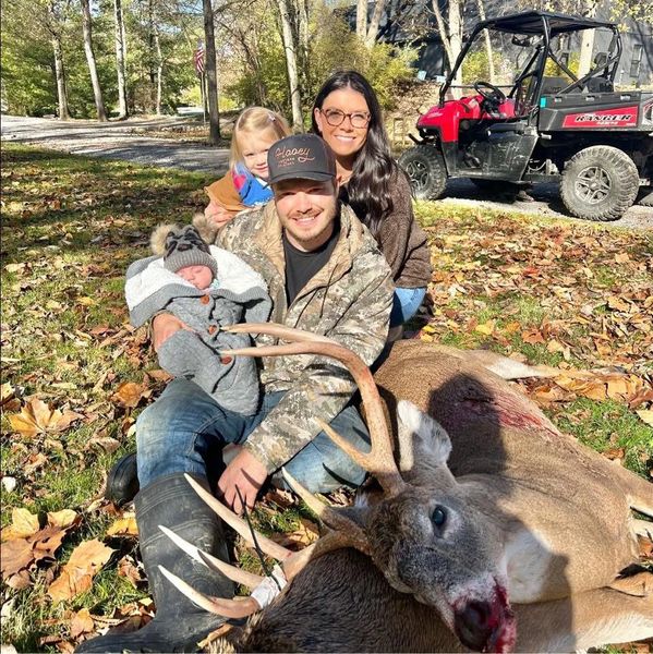 Family posing outdoors with a hunted deer on a sunny day.