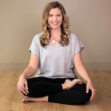 Smiling woman sitting cross-legged on wooden floor in a relaxed pose.