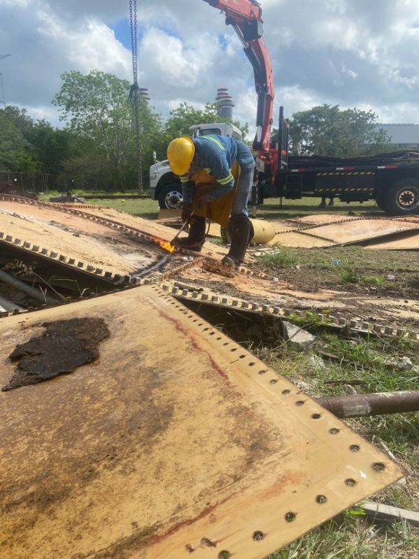 Trabajador con equipo de protección usando herramienta de corte en metal oxidado.