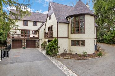 A large beige Tudor-style house with round turret and double garage.