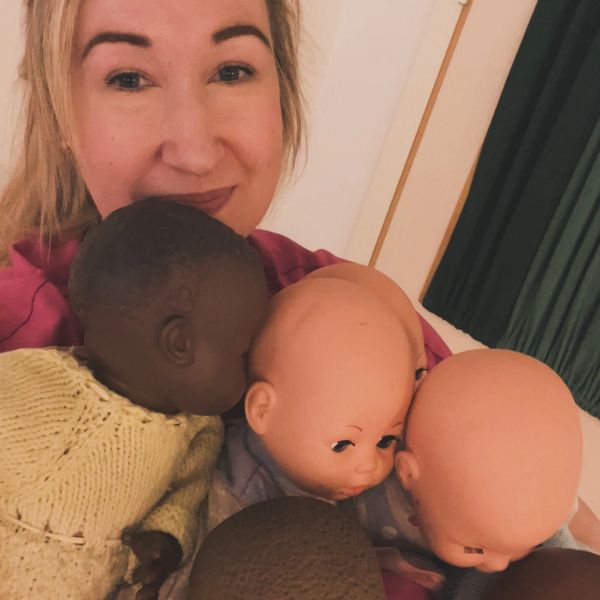 Healthcare professional smiling with several baby dolls around her.