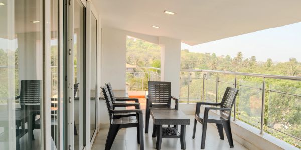 Modern balcony with black chairs and table overlooking greenery.