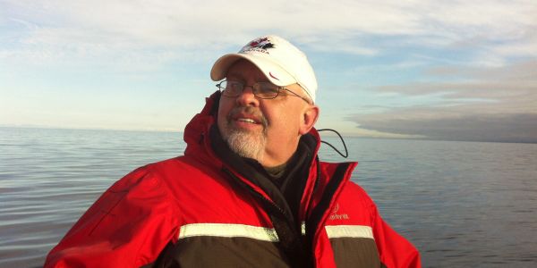 Man in red jacket and white cap on a boat.