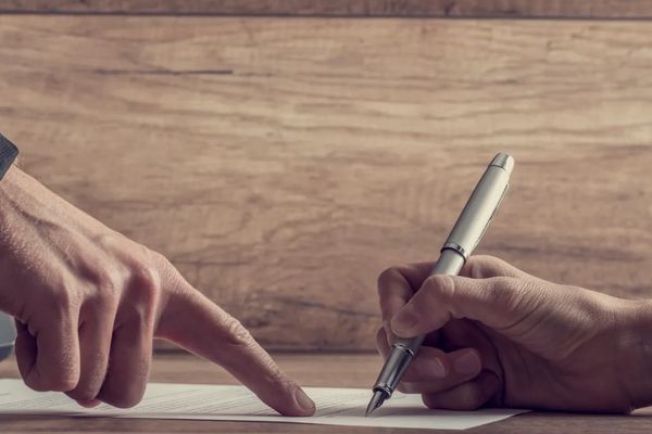 Sales deals closing faster with one hand signing a contract in the oplace where another hand is poin