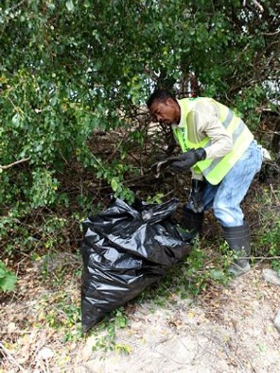 Man in safety vest cleaning outdoor area with black garbage bag.