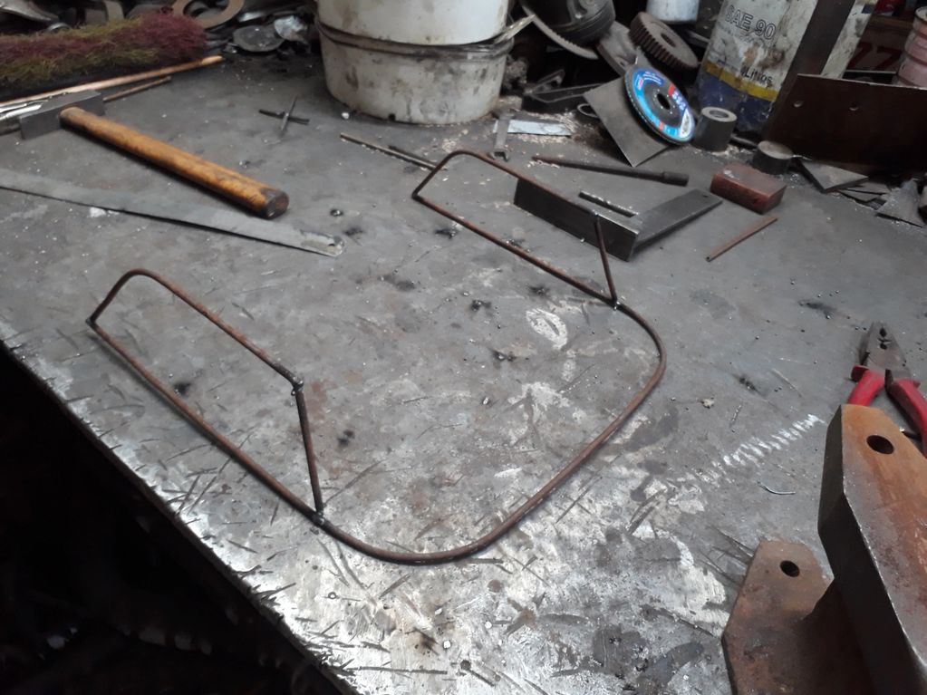 A metal workshop table with tools and a bent wire frame.
