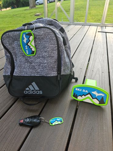 Gray Adidas backpack with Ski Da tags and a car key on wooden deck.