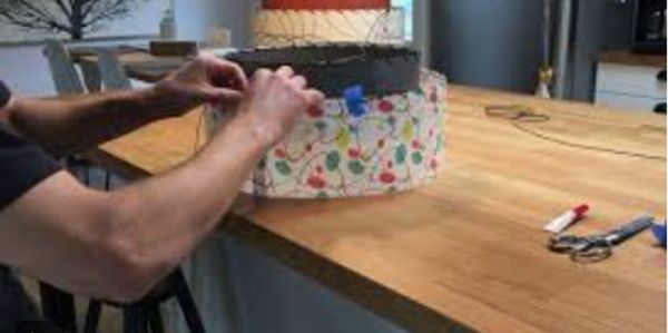 Person crafting a colorful wire and bead basket on a wooden table.