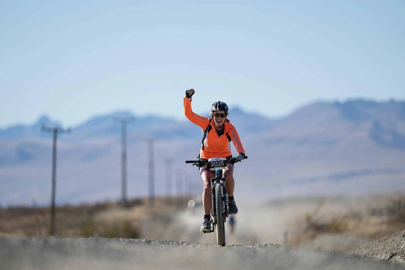 Cyclist celebrating victory on a gravel road in a mountainous area.