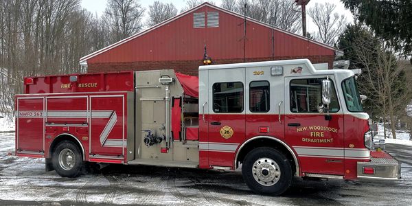 Red New Woodstock Fire Department fire truck parked outside a barn.