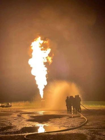 Firefighters combat a large fire flame at night.