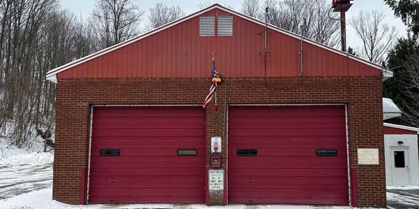 Red fire station building with two garage doors in a snowy setting.