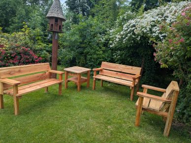 Wooden garden benches and table set on green lawn surrounded by flowering bushes.