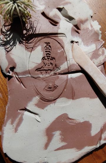 Clay slab with a carved seal and sculpting tool on a wooden surface.